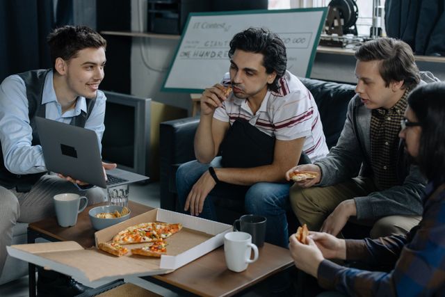 Group of young men having pizza and discussing ideas during a startup meeting in a casual setting. Related image for Hospitality Startups: How Brands Can Improve Performance.