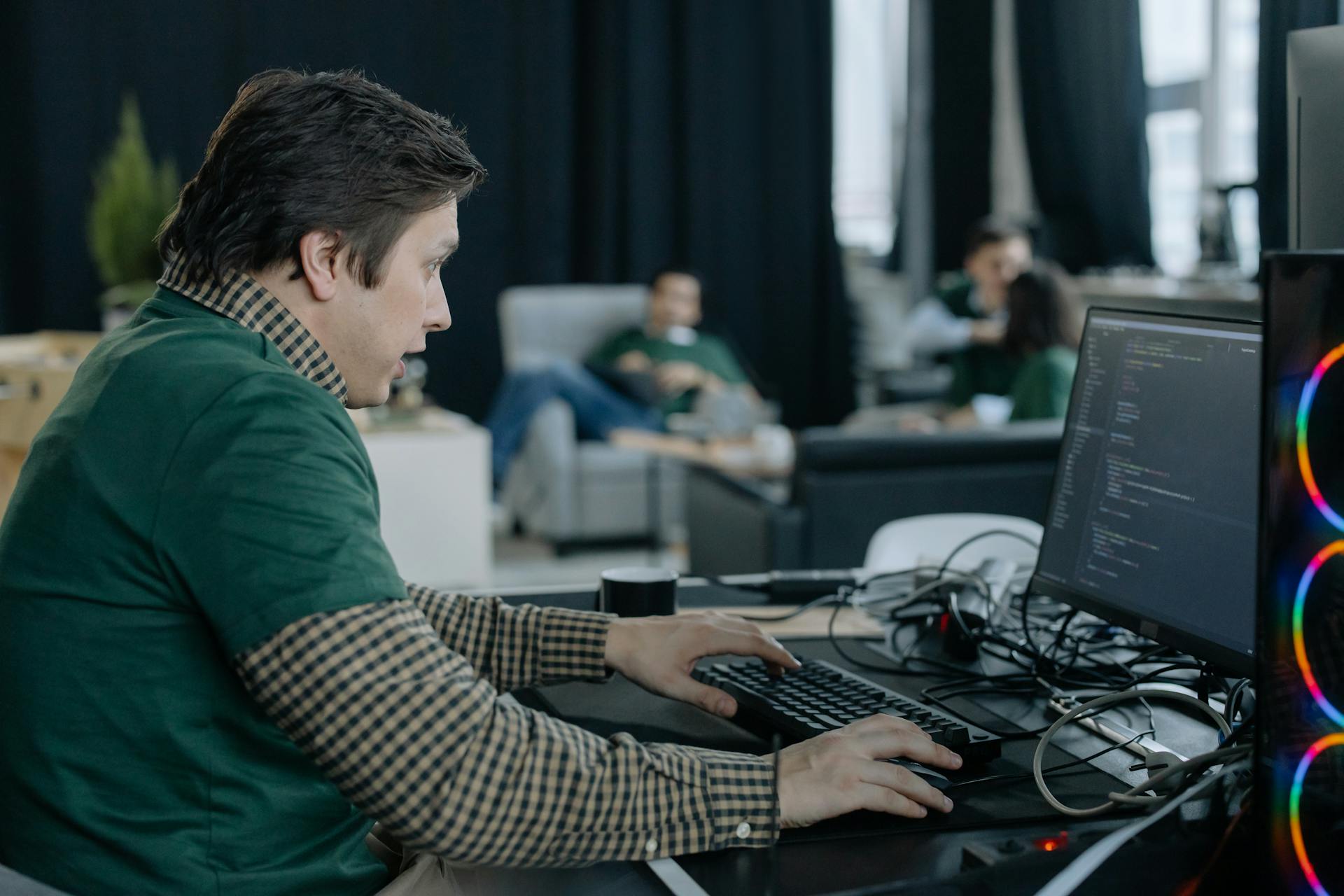 Male programmer concentrating on coding at a computer in a contemporary office setting.