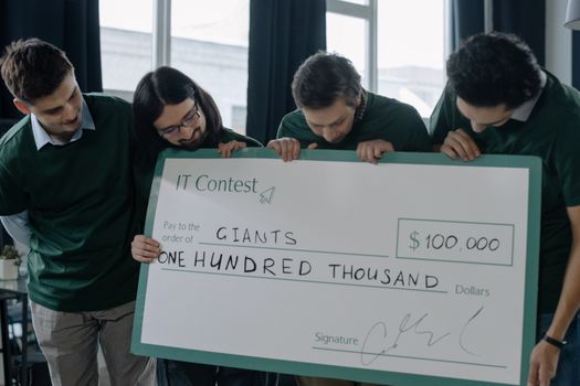 Excited startup team holding a $100,000 check after winning an IT contest, showcasing their success.