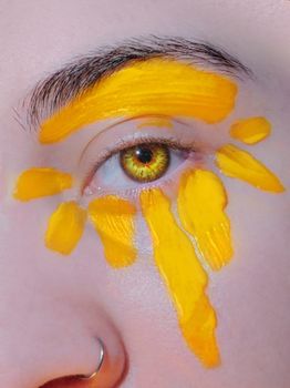 Close-up of an eye with creative yellow face paint strokes for artistic effect.