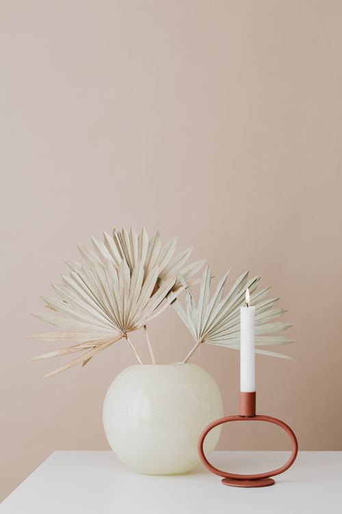 Free A minimalist setup featuring a sleek candle holder and a vase with dried palm leaves. Stock Photo