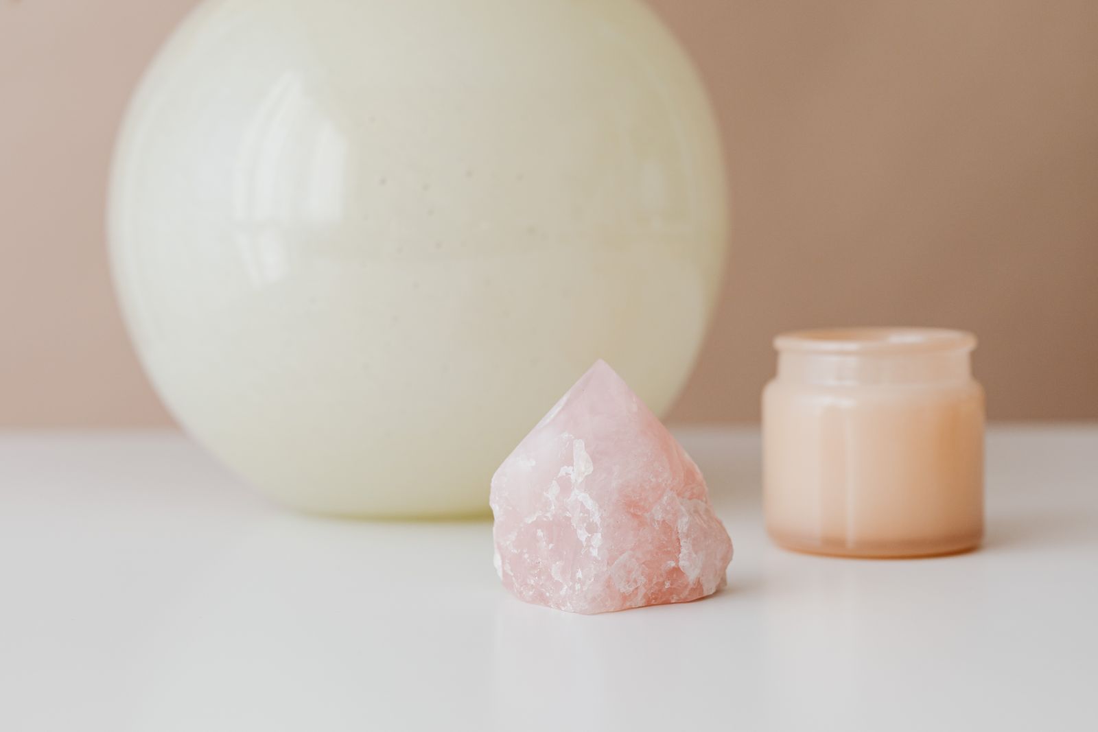 Rose quartz crystal stone and lit candle arranged on a soft neutral background