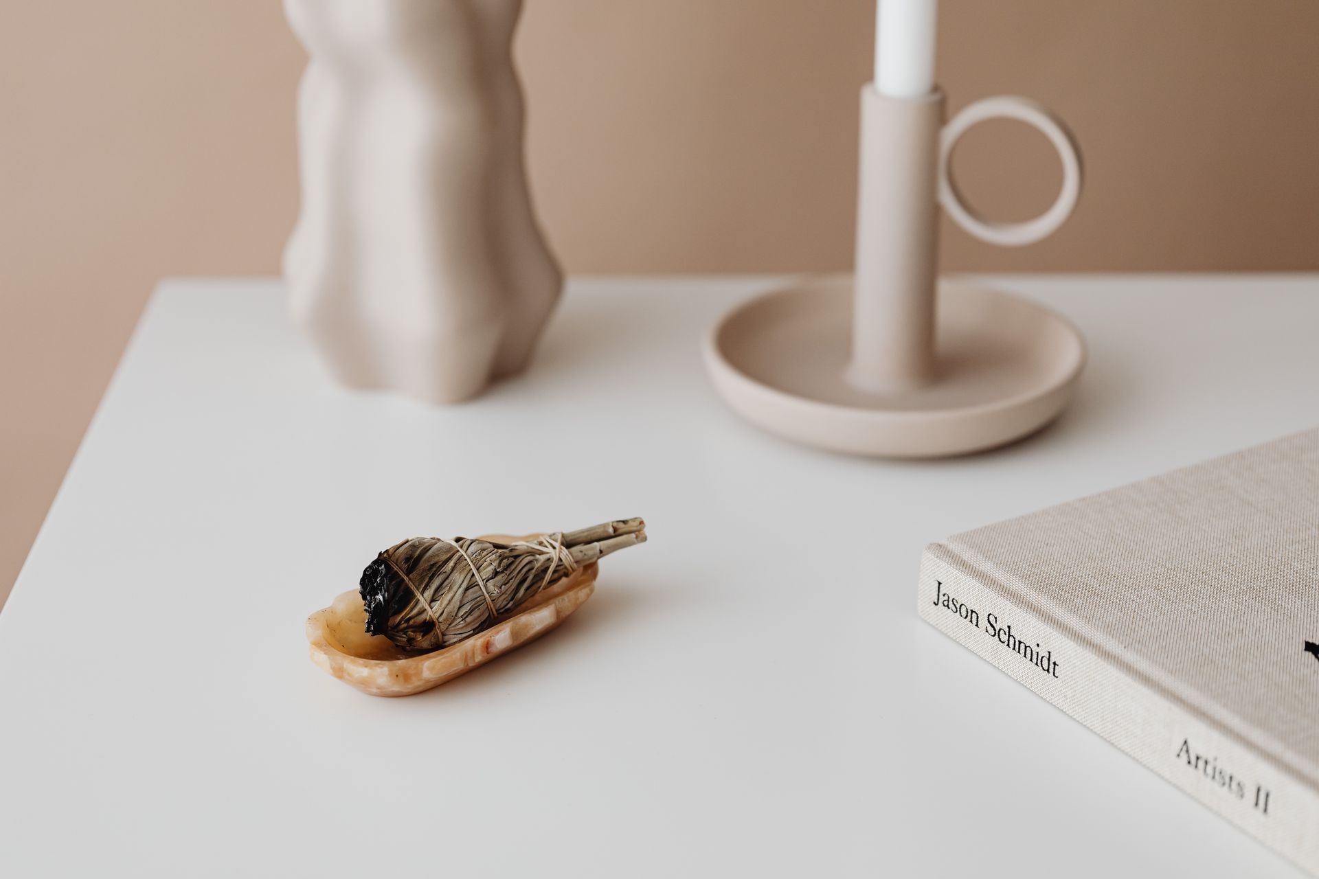 Elegant minimalist setup featuring a sage bundle, candle, and decorative objects on a white surface.