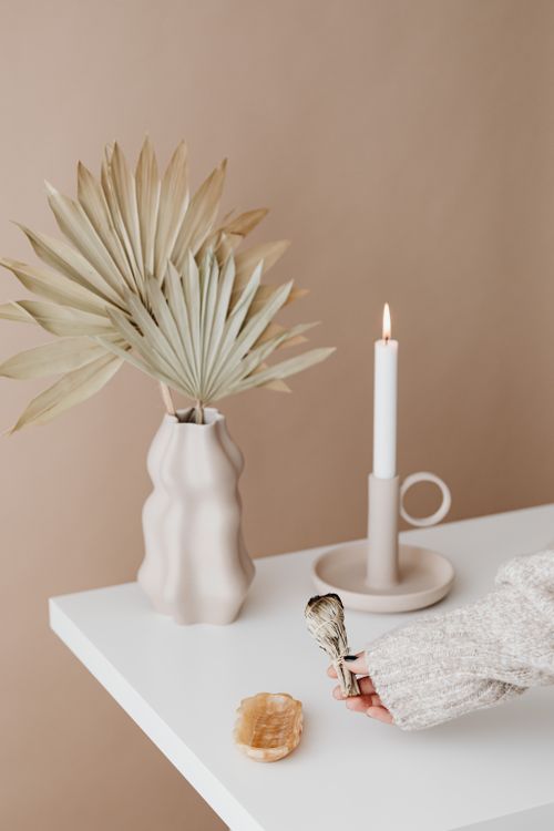 Free Elegant minimalist setup featuring a burning candle, dry palm leaves in a vase, and incense on a white table. Stock Photo