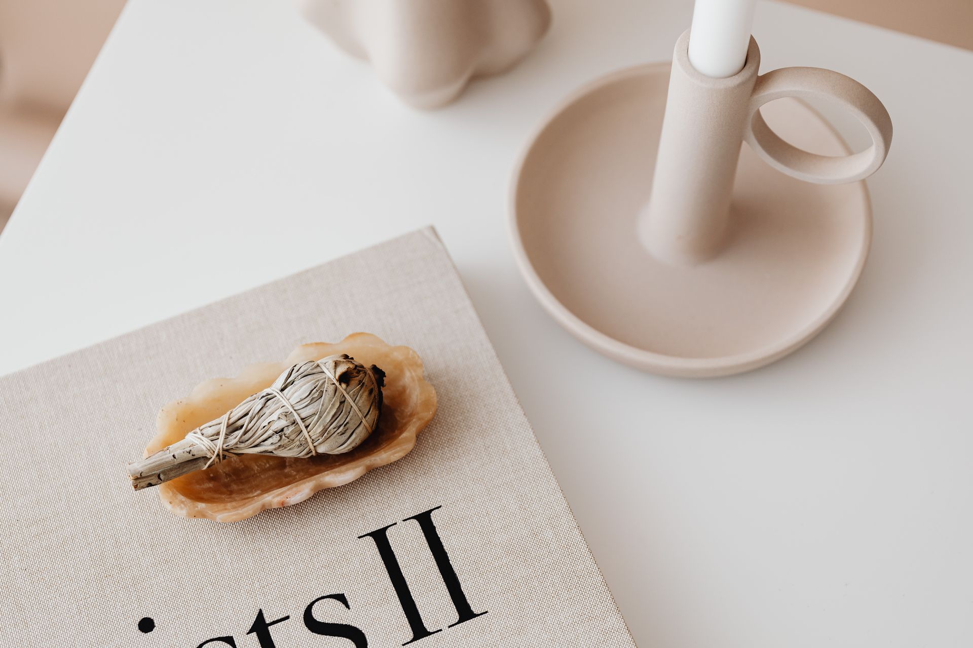 A minimalist home decor arrangement featuring a candle holder and sage bundle on a white table.