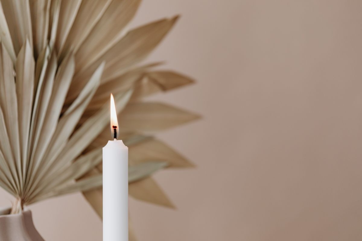 A white candle burning in front of dried palm leaves