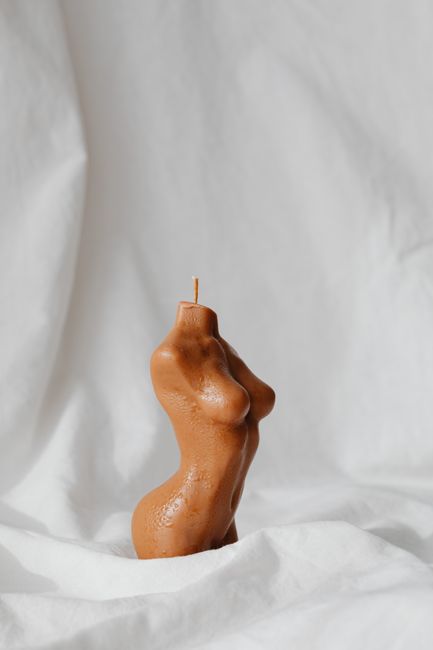 Aesthetic candle shaped like a female torso on minimalist white fabric background.