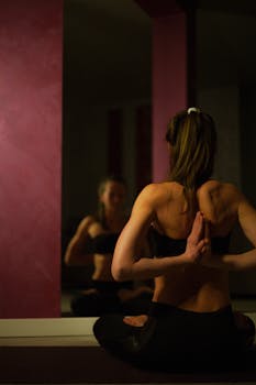 Back view of a woman practicing yoga, focusing on balance and flexibility in a dimly lit room.