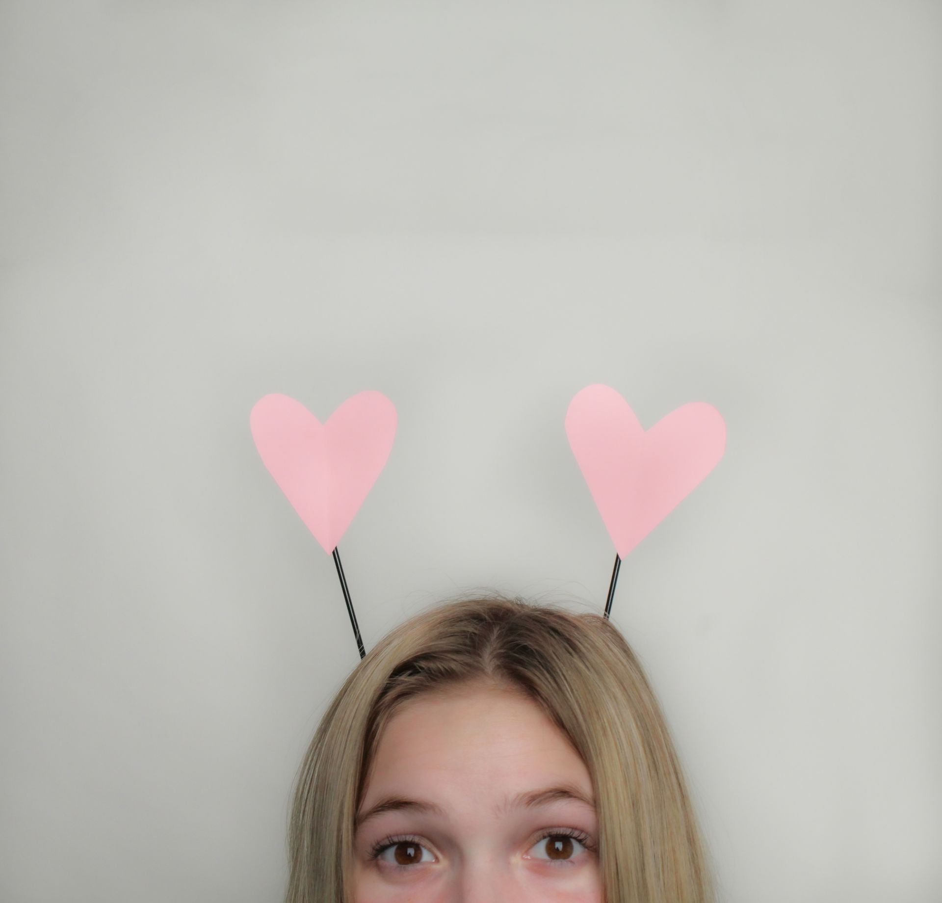 A young blonde girl wearing a playful heart-shaped antenna headband.