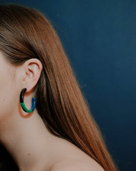 Close-up portrait of a woman wearing a colorful hoop earring against a blue background.