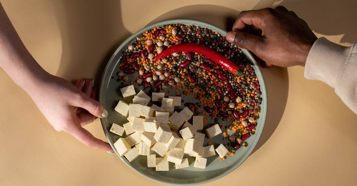A diverse plate with tofu, legumes, and a chili pepper. Hands shown.