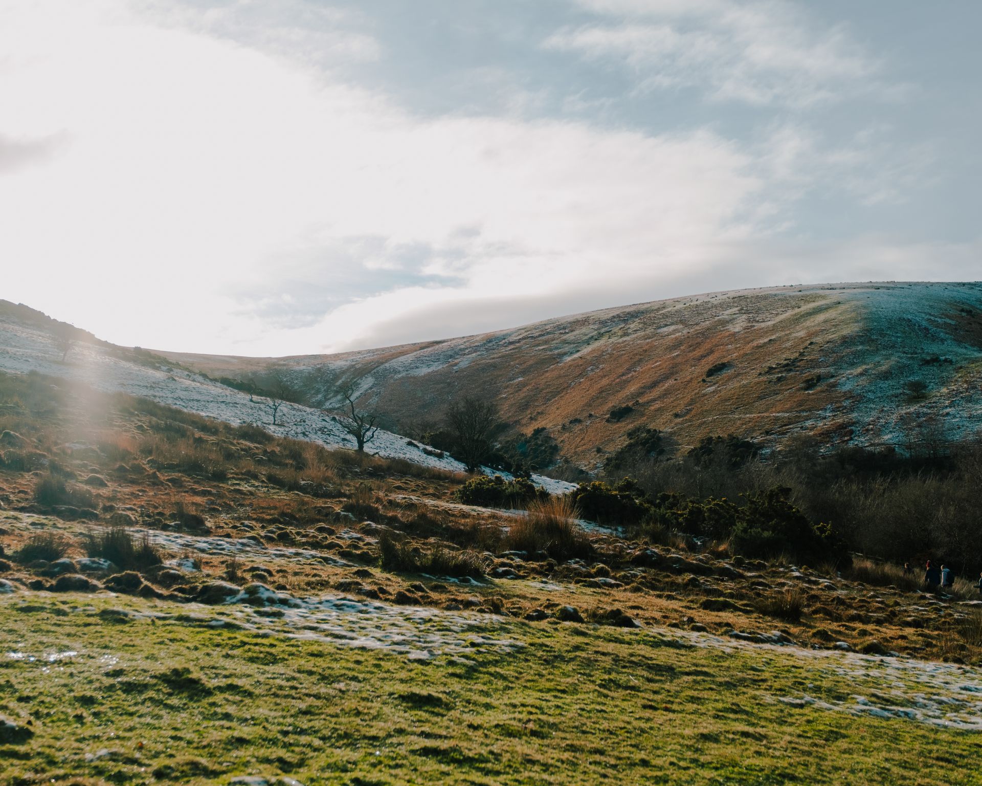 Gently sloping hillside with snow patches and grassy terrain under a bright and cloudy sky.