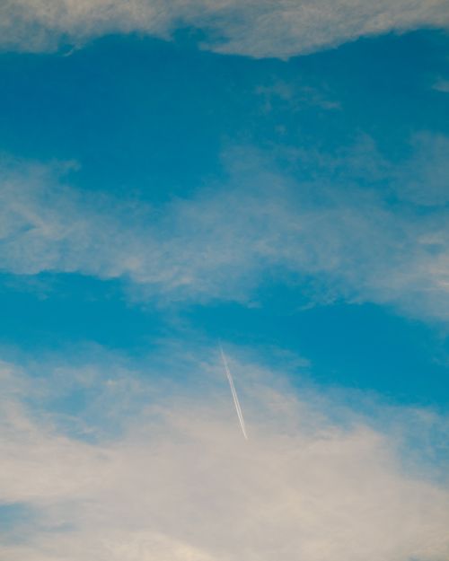 Free A high-altitude airplane leaves a vapor trail against a clear blue sky with scattered clouds. Stock Photo