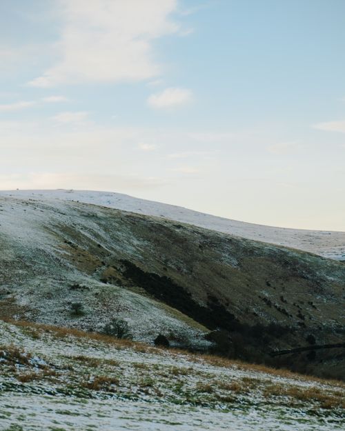 Free A serene landscape of rolling hills dusted with snow under a bright blue sky. Stock Photo