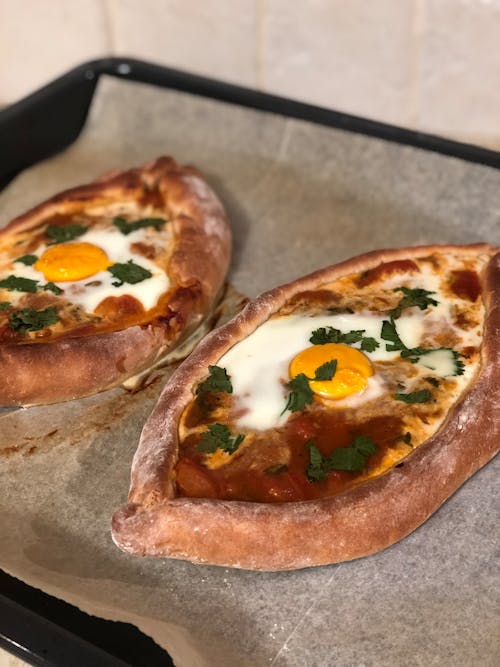 From above of freshly baked khachapuri with cheese and eggs decorated with herbs placed on baking pan with baking paper