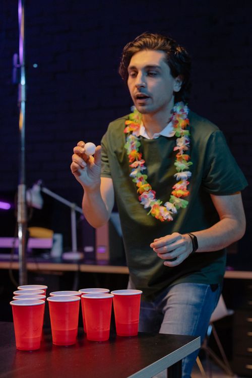 Free A young man playing beer pong during an indoor party, wearing a floral lei and casual clothes. Stock Photo