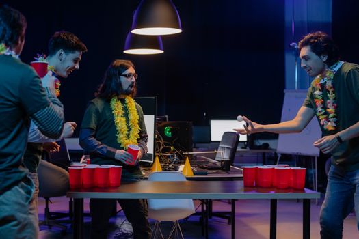 Group of coworkers playing beer pong in a fun office setting at night.