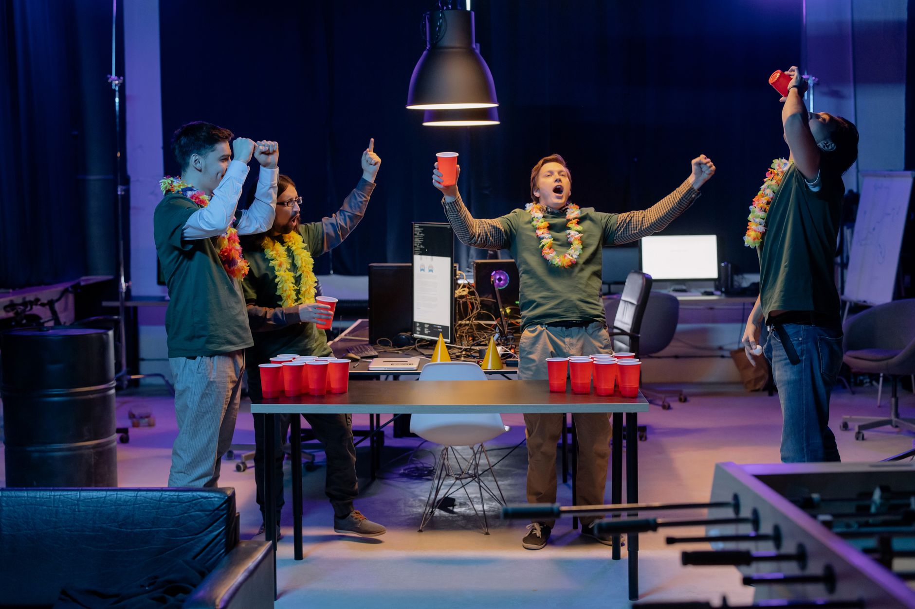 A group of friends playing beer pong indoors, celebrating with red cups and leis around their necks.