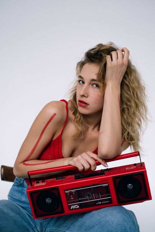 Free Stylish woman in red top and jeans holding a retro red tape recorder in a studio setting. Stock Photo