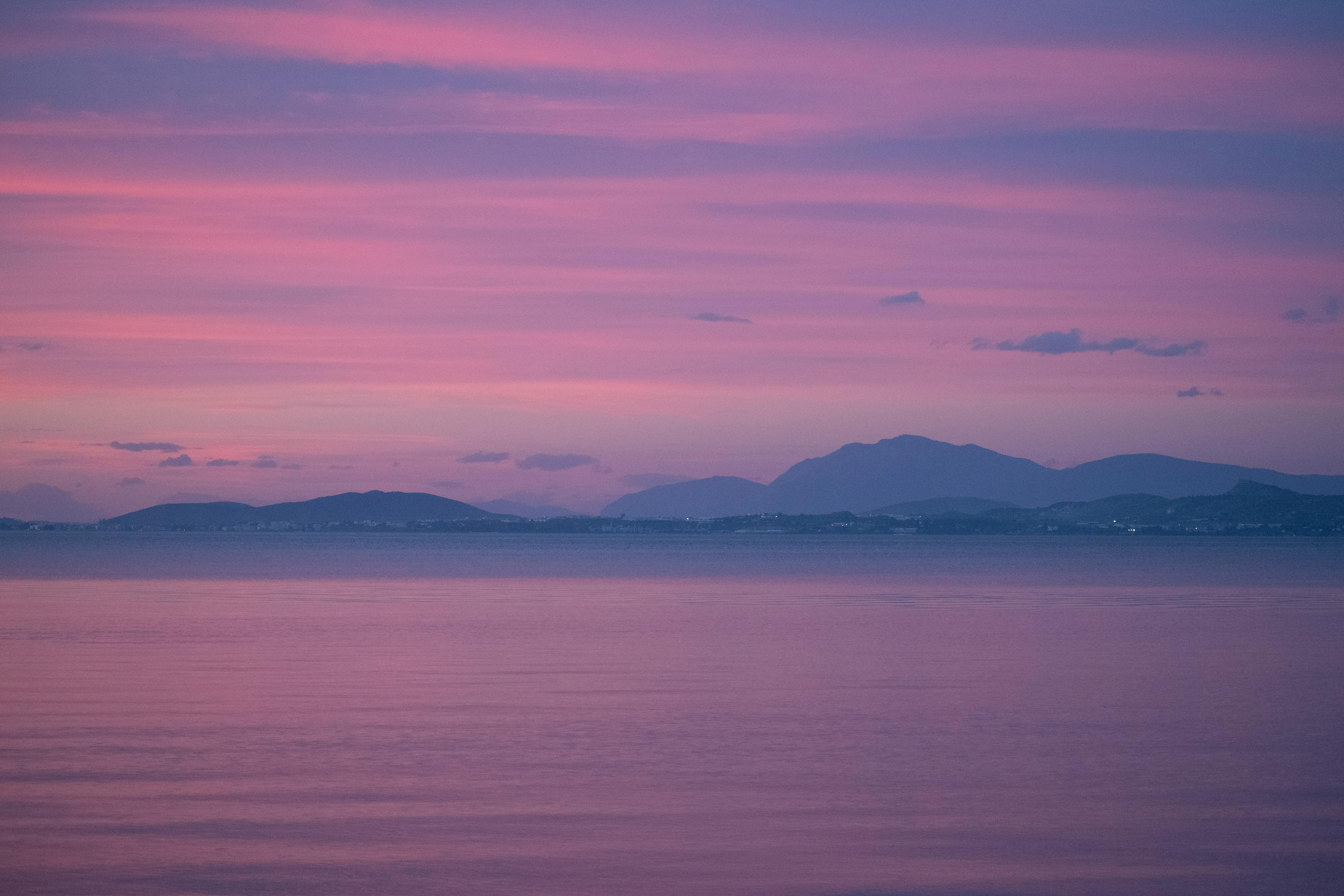 Tranquil pink sunset over a calm sea in Greece, showcasing stunning natural beauty and serenity.