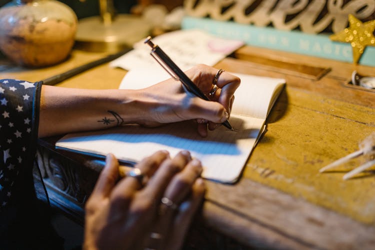 A Person Writing On A Notebook