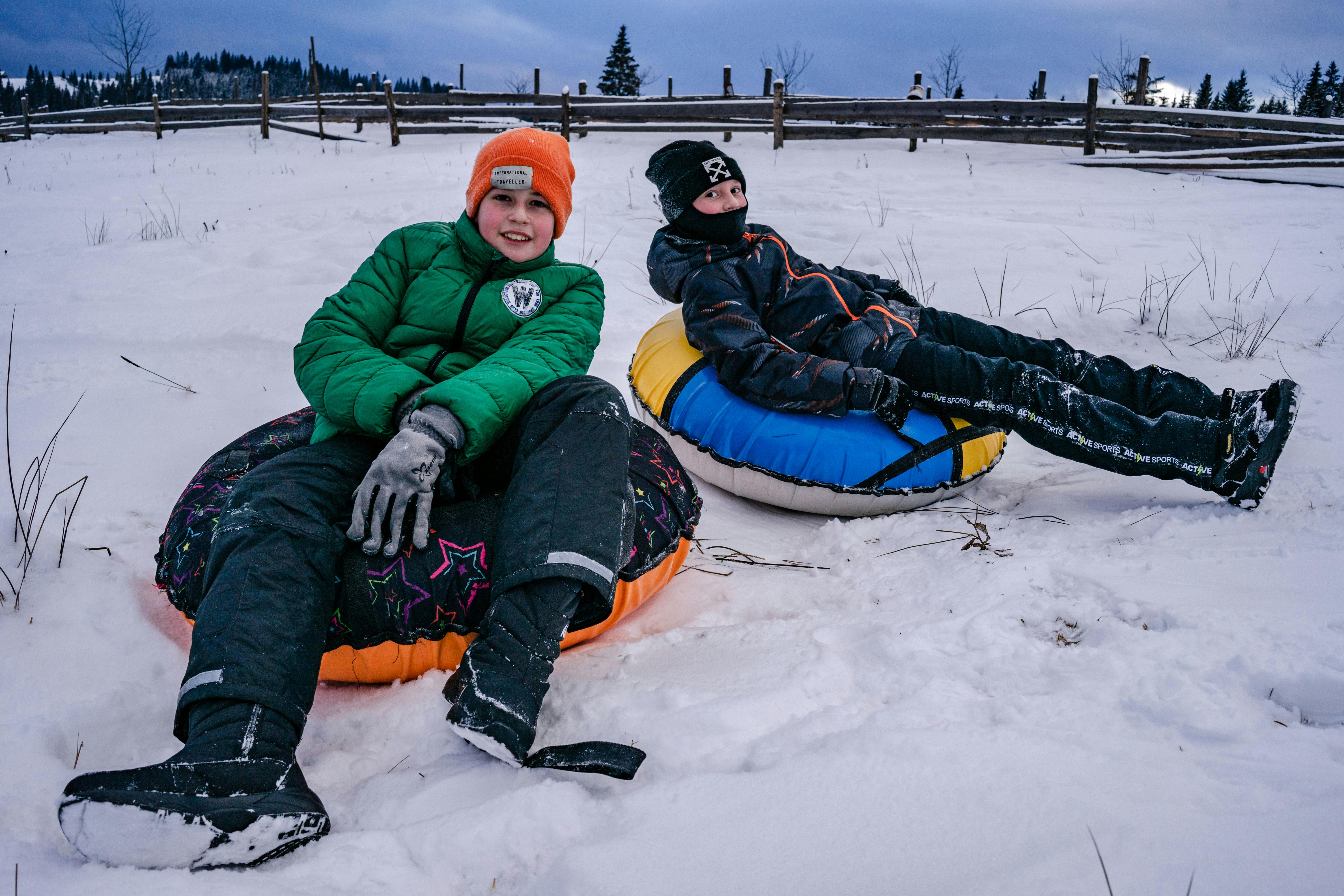 happy boys in outerwear on tubes in snow