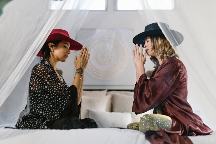 Women Wearing Hats Sitting On A Bed Praying