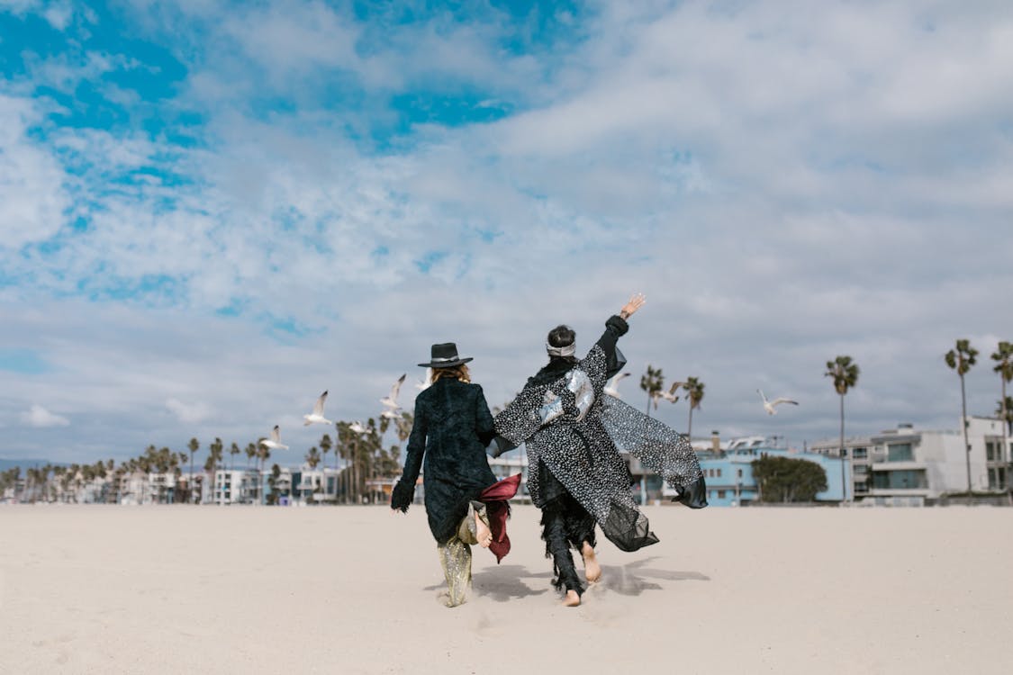 Man and Woman Walking on White Sand Under Blue Sky