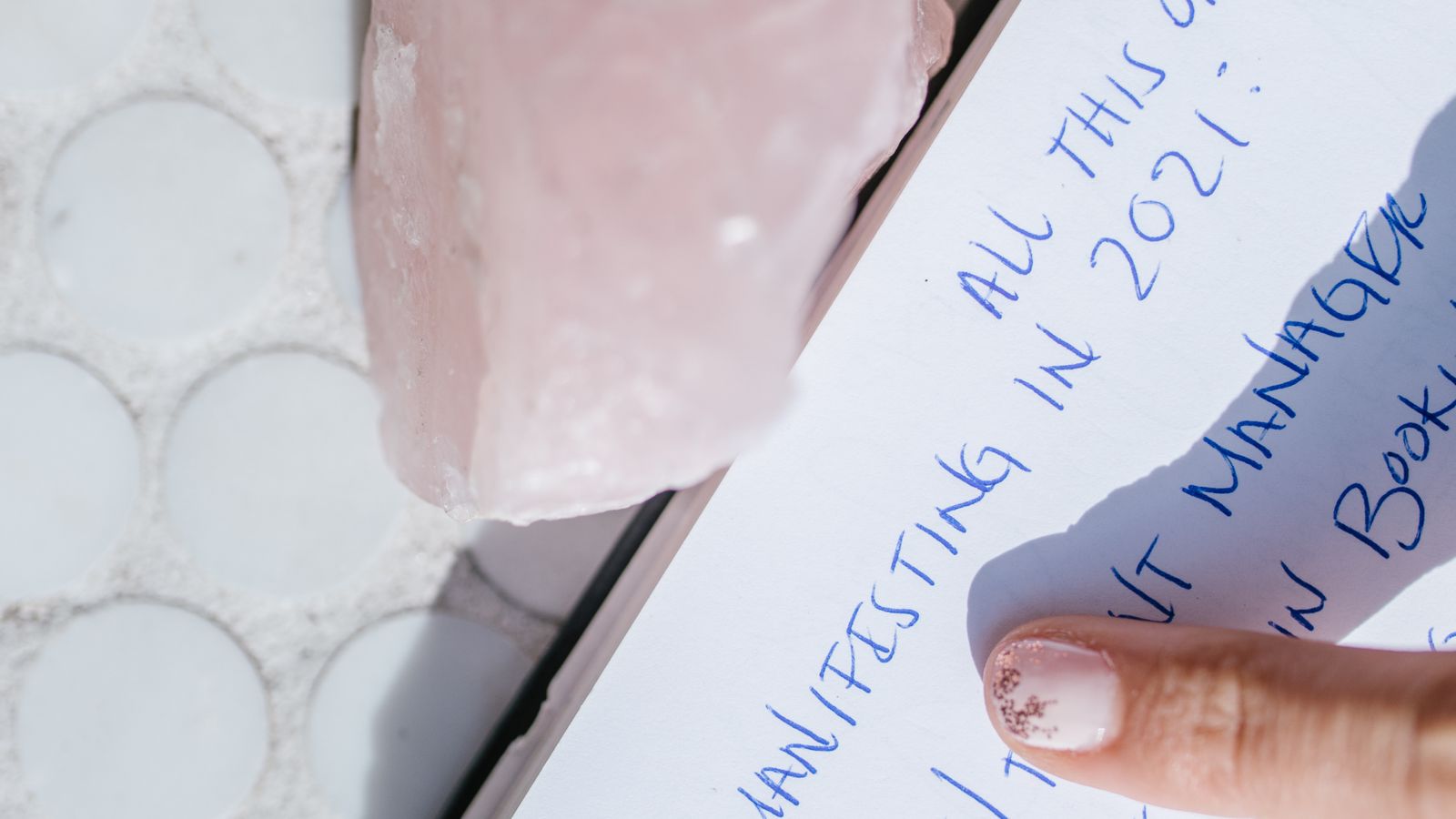 Close-up of a manifestation journal page with a rose quartz crystal and a finger pointing