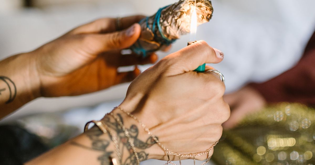 Close-up of tattooed hands lighting Palo Santo during a spiritual ritual indoors.