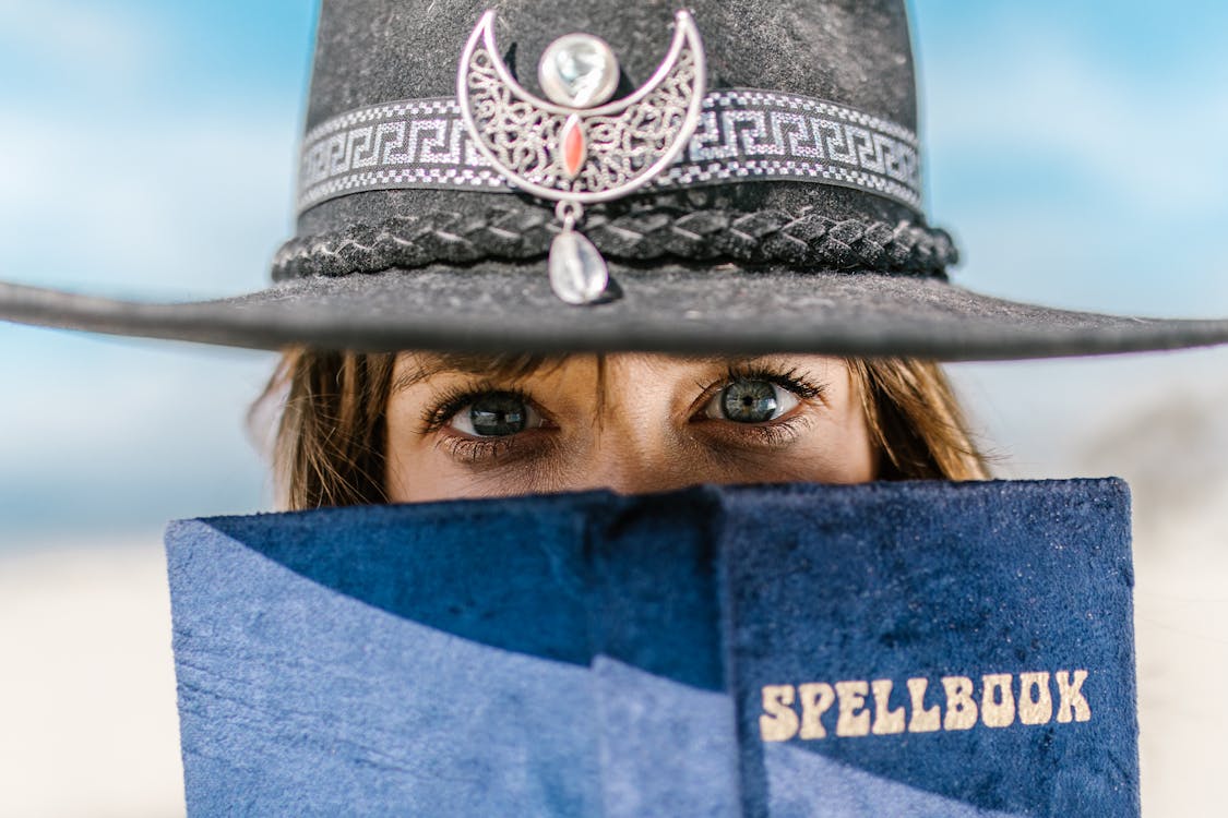 Free Close-up Shot of a Person in Black Hat Holding a Spell Book while Seriously Looking at the Camera Stock Photo