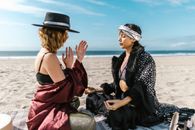 2 Women Sitting on Gray Rock Near Sea