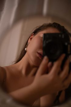 Faceless female in bra with photo camera taking selfie of reflection in mirror in light apartment