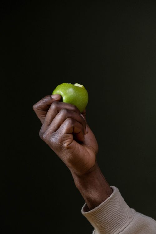 Free A detailed view of a hand raising a bitten green apple against a dark background. Stock Photo