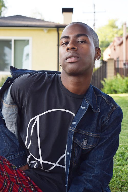 Free Confident young African American male in earrings looking at camera on lawn against houses in daytime Stock Photo