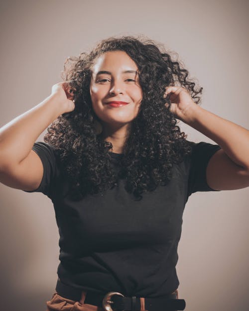 Free Beautiful Woman in a Black Crew Neck Shirt Touching Her Curly Hair Stock Photo