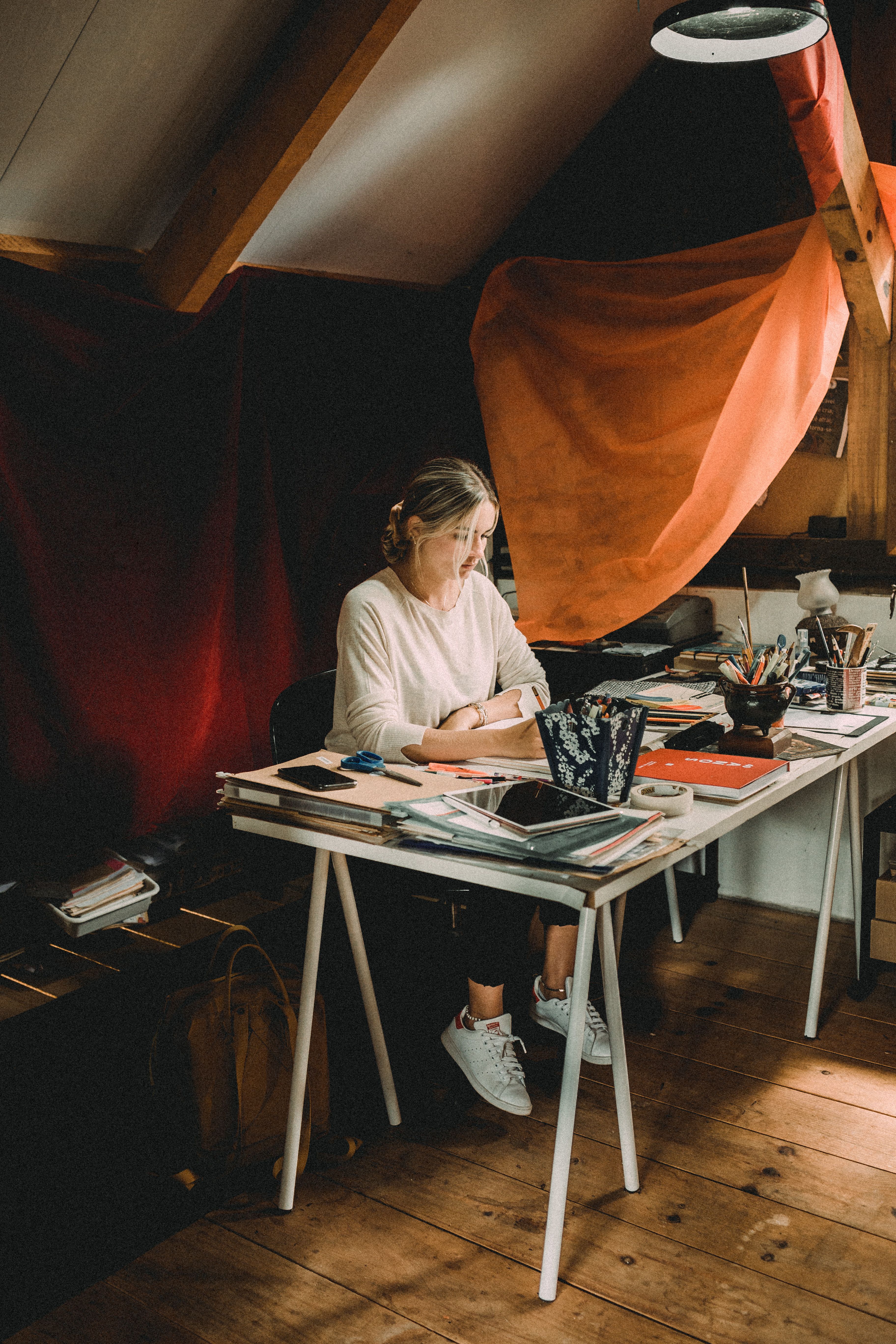 Young serious female drawing at table with different art tools in modern workshop