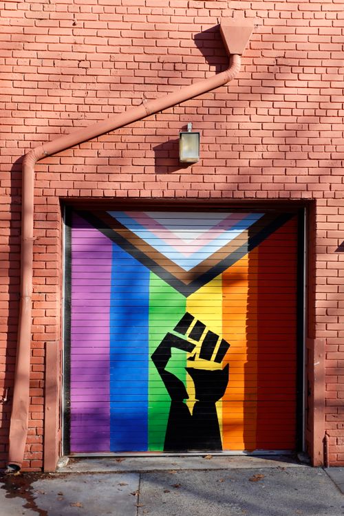 Free Colorful street art on a garage door with a raised fist and Progress Pride Flag in Sacramento. Stock Photo