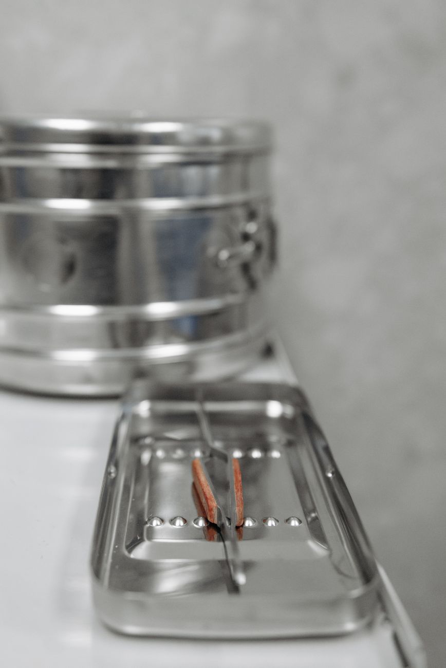A sterilized dental instrument resting in a steel tray beside a sterilization drum in a dental office