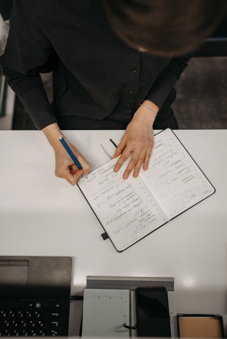 Person Sitting At Table Writing On Diary