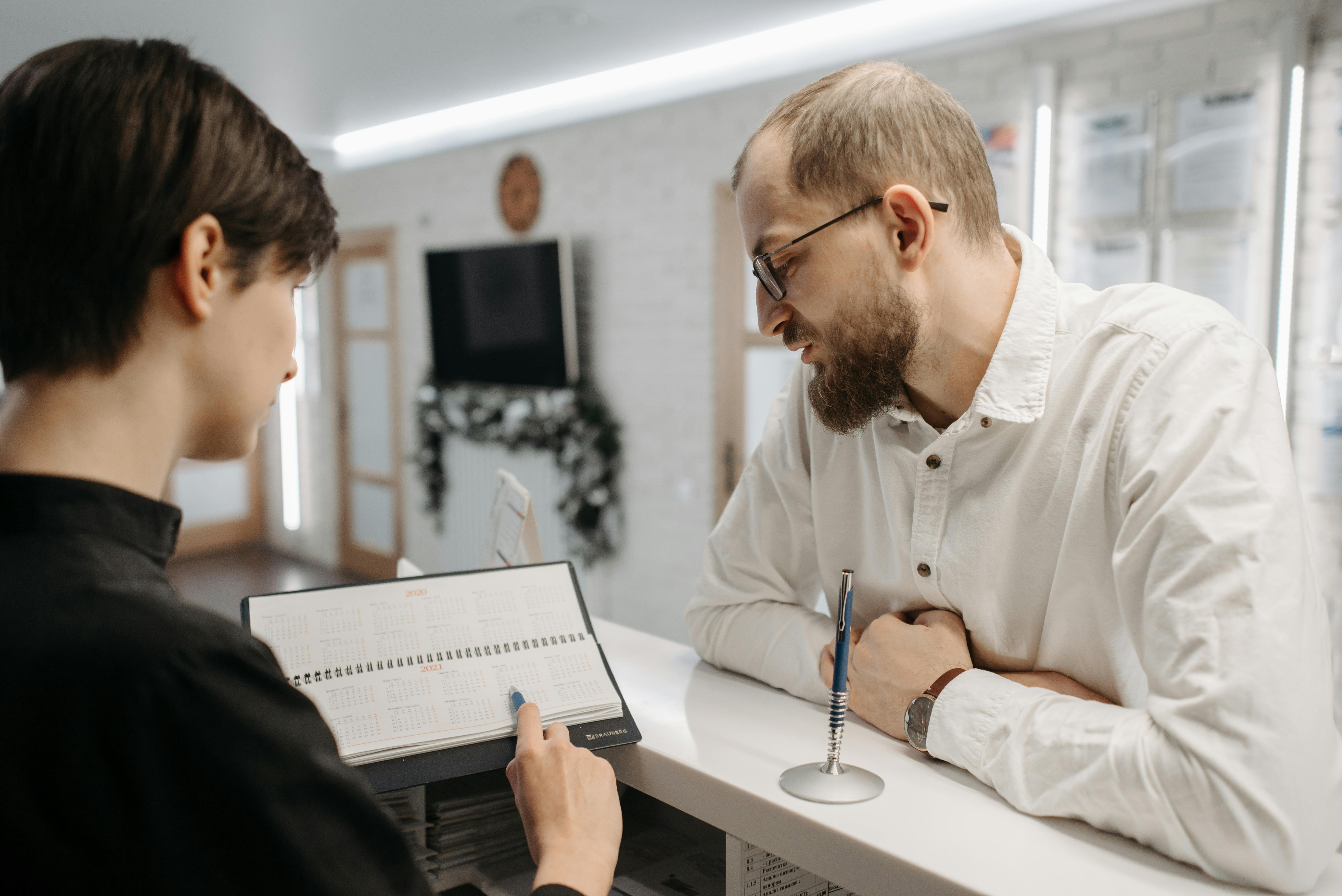 woman at reception desk showing a calendar to a man