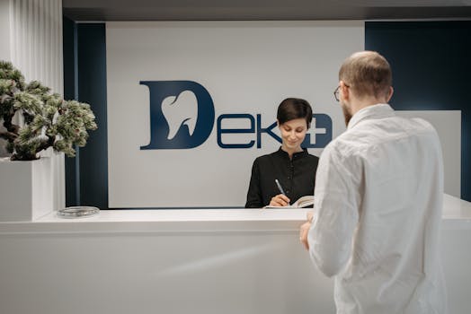A receptionist assisting a patient at a dental clinic counter, with a potted plant in sight.