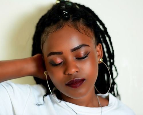 Free Close-up portrait of woman with dreadlocks, hoop earrings, and striking makeup on a light background. Stock Photo