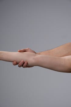 A close-up image of two hands holding in a supportive gesture on a neutral background.