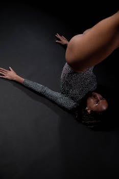 Young female gymnast performing a flexible pose on a dark stage, showcasing strength and elegance.