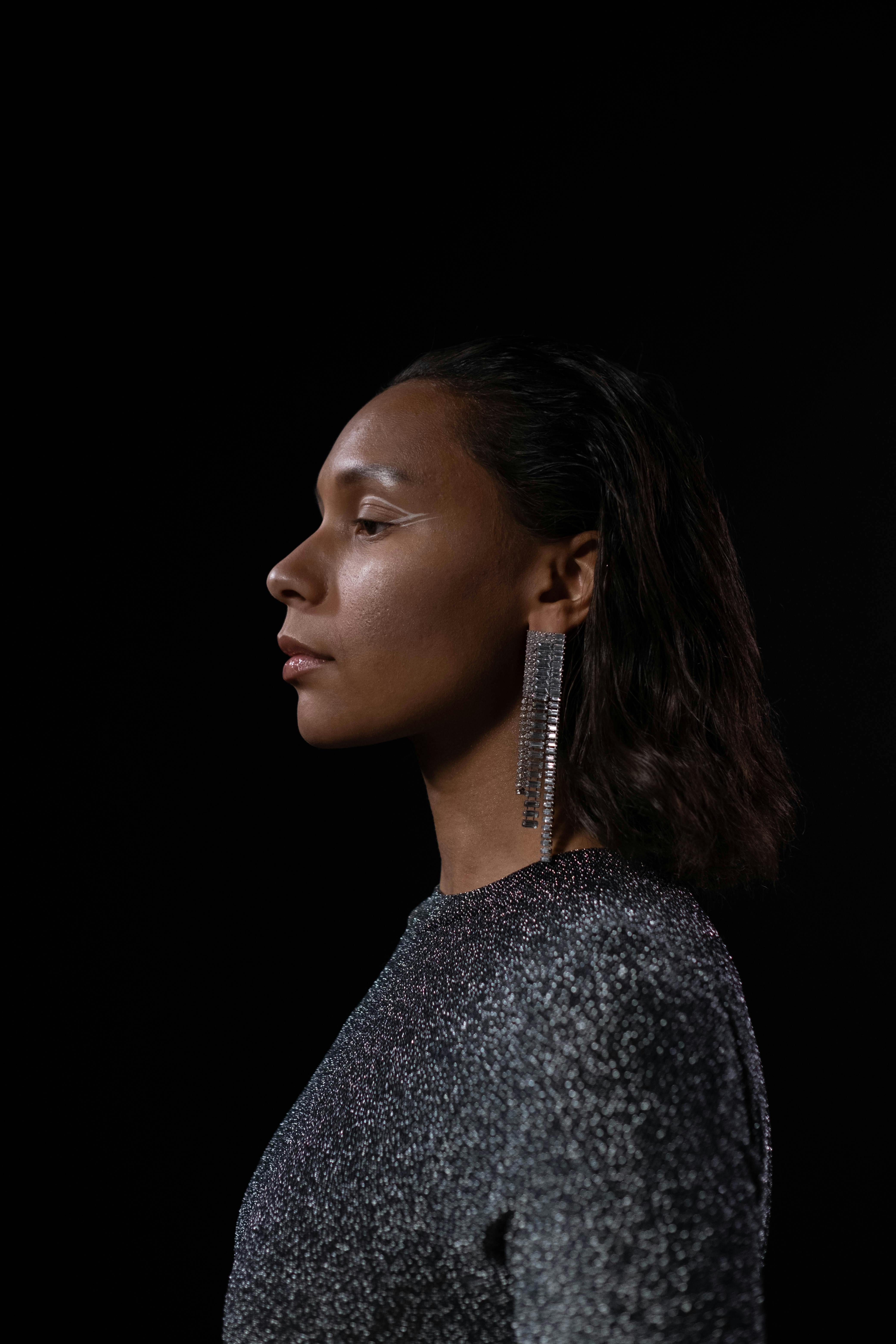 Side view portrait of a woman in glamourous fashion with statement earrings on a black background.