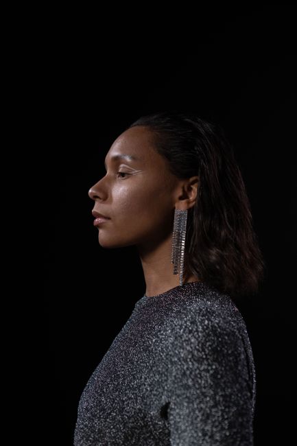 Side view portrait of a woman in glamourous fashion with statement earrings on a black background.