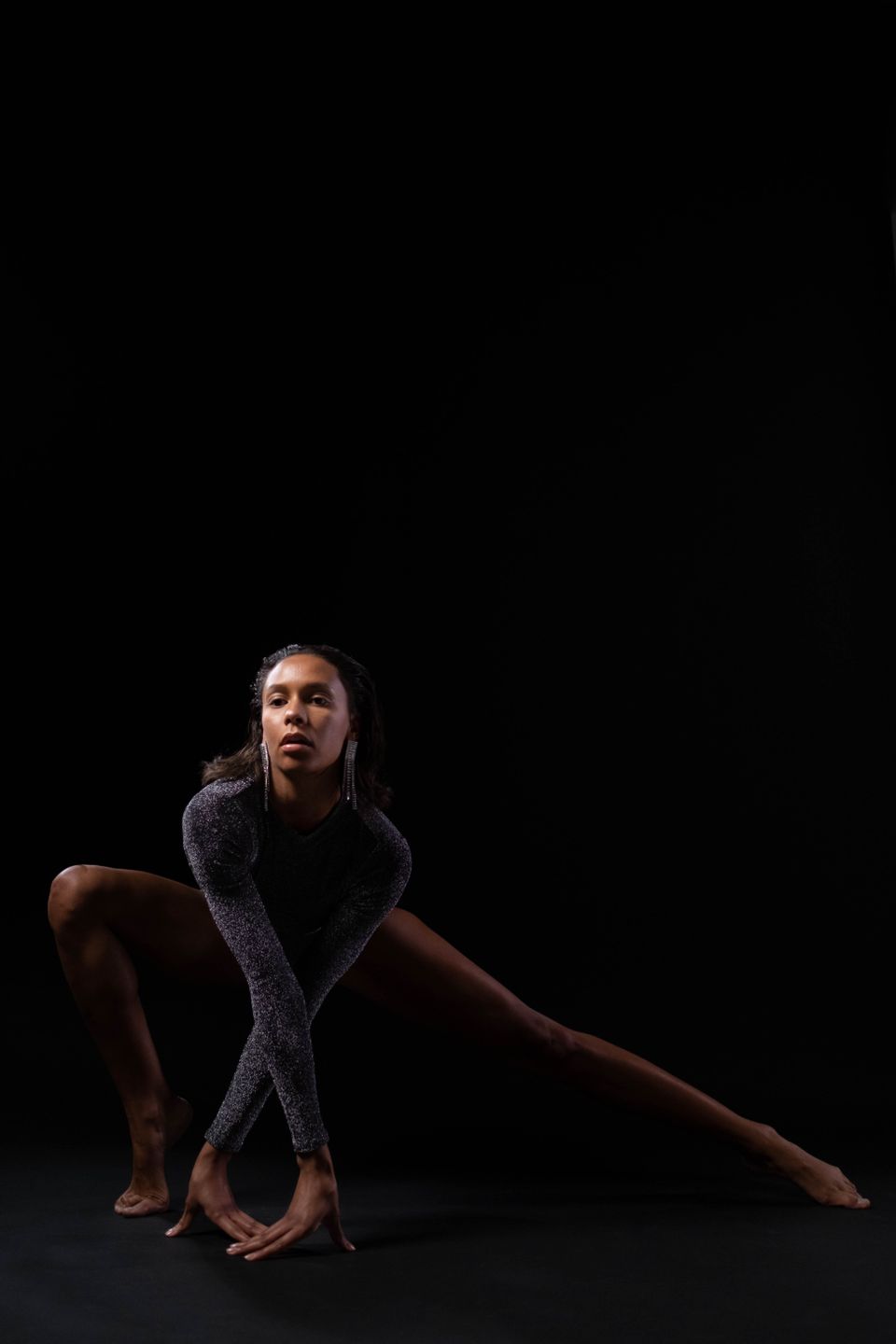 Athlete holding a low stretch against a black studio backdrop — cottonbro studio on Pexels