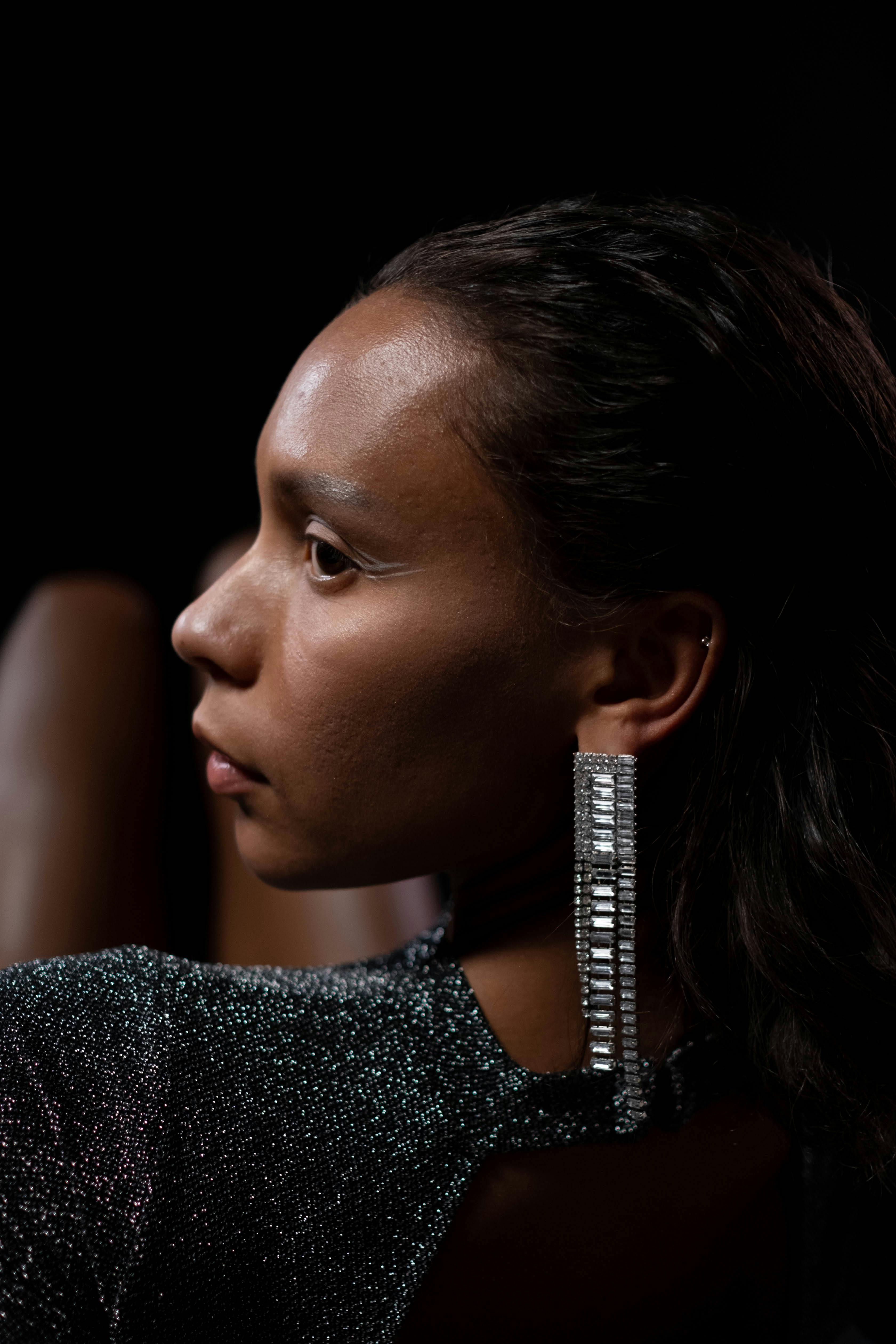 A sophisticated portrait of a woman wearing sparkling earrings, showcasing elegance against a dark background.