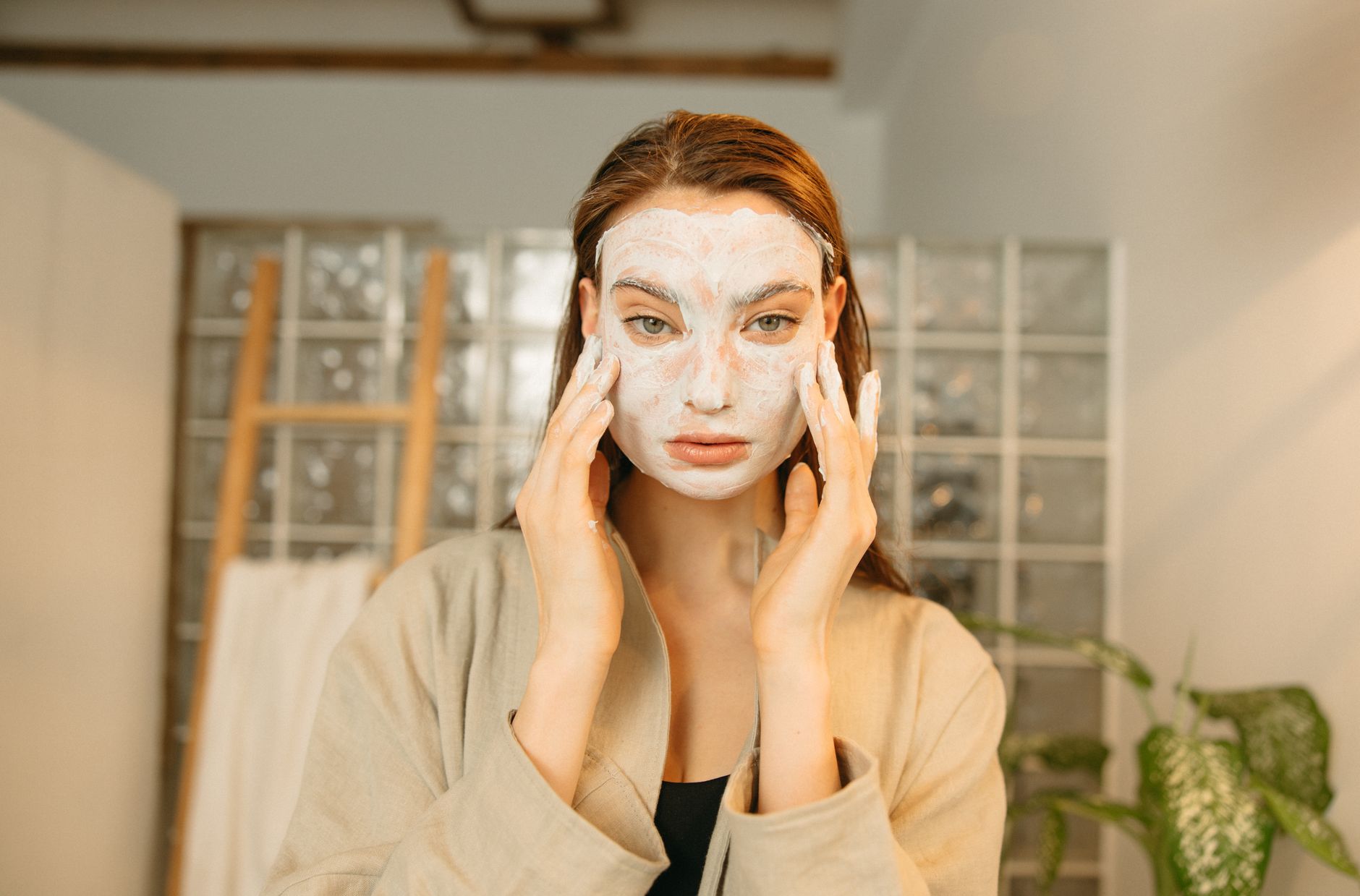 Woman applying a cosmetic face mask for skincare relaxation indoors. Ideal for beauty and wellness concepts.
